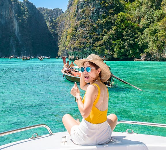 Woman on speedboat in turquoise waters of Phi Phi Island, surrounded by cliffs.
