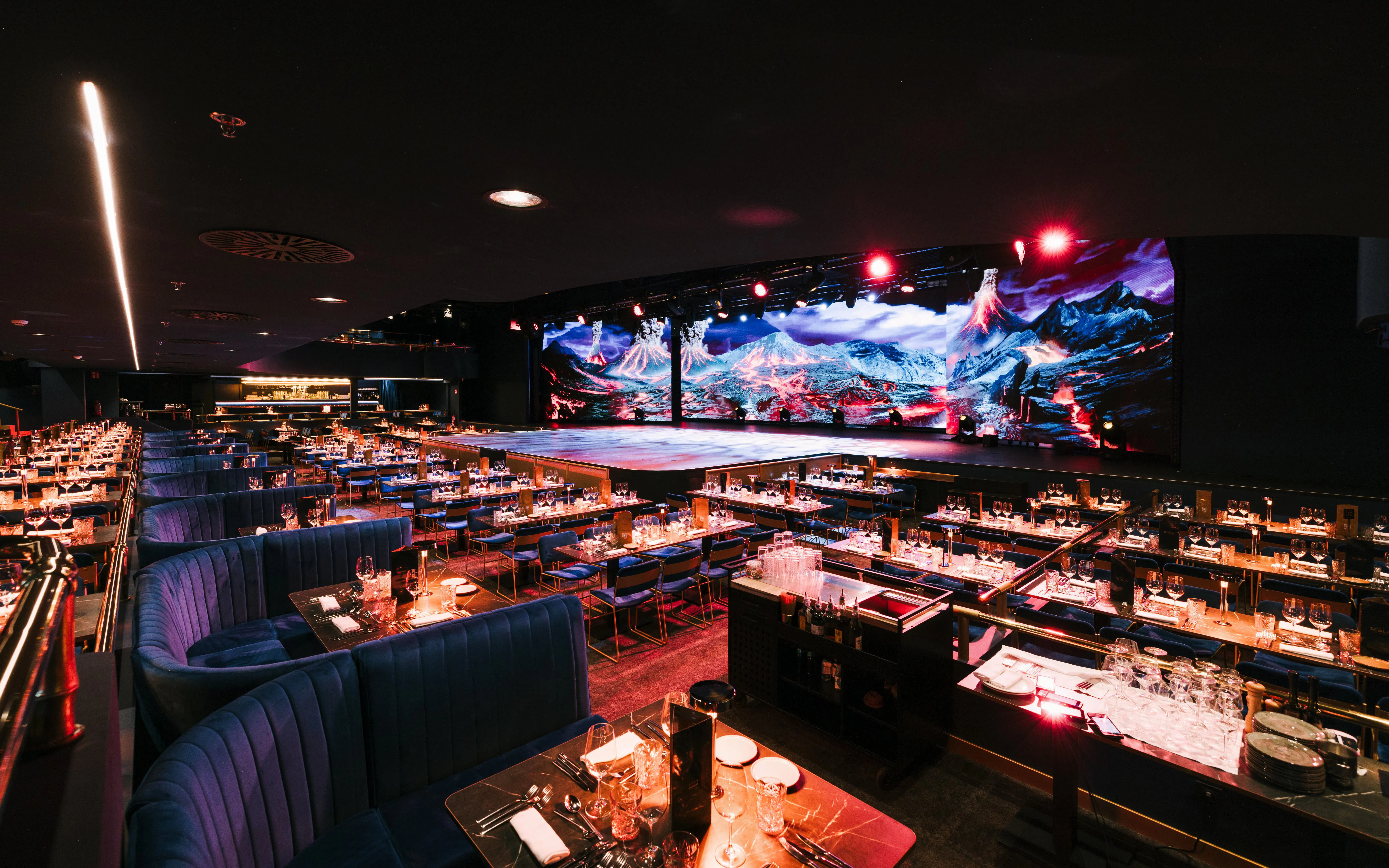 Seating area with tables set for dining at Sala Scala, Gran Canaria, facing a stage with vibrant backdrop.