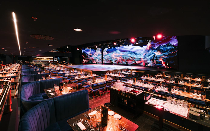 Seating area with tables set for dining at Sala Scala, Gran Canaria, facing a stage with vibrant backdrop.