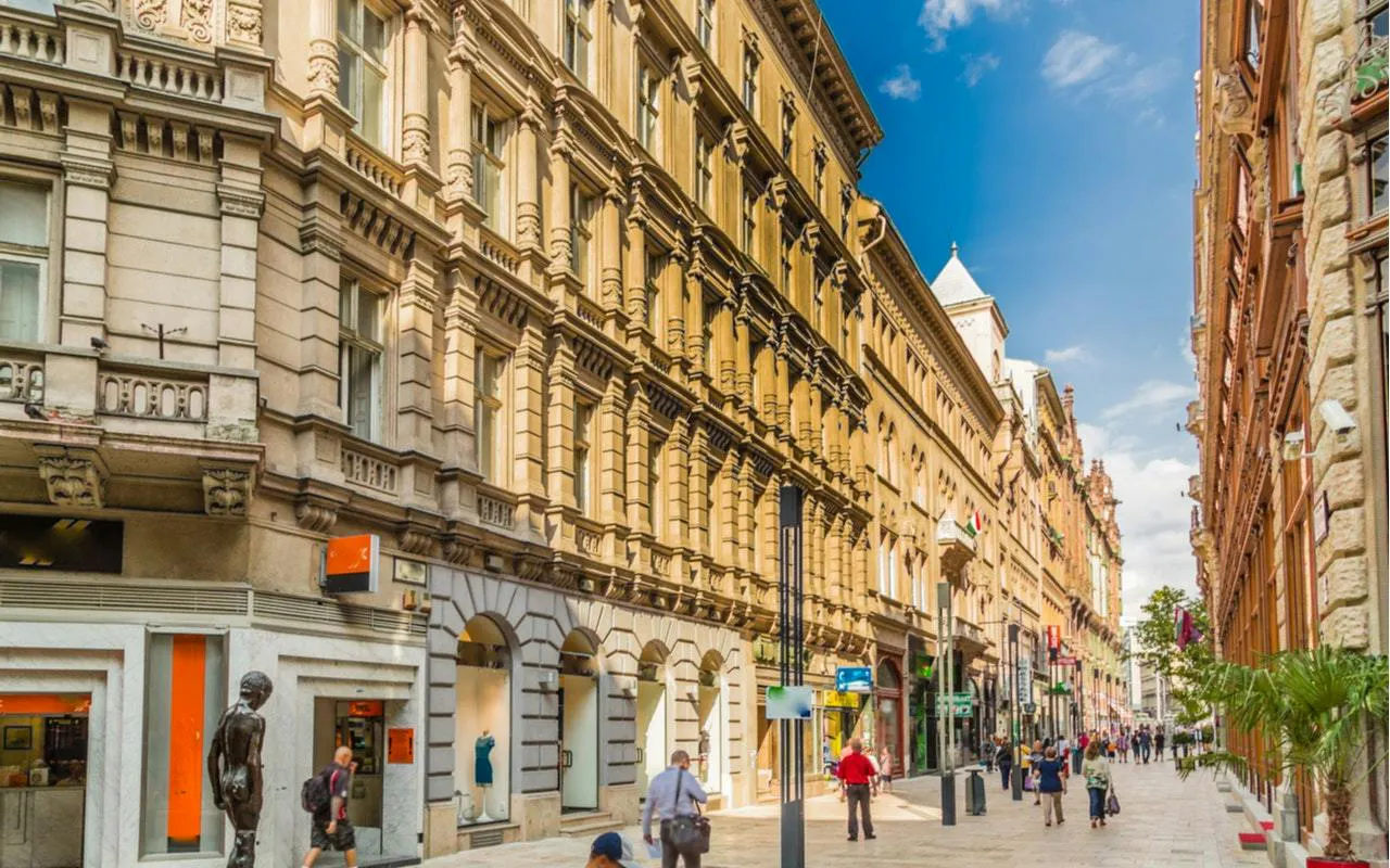 Pedestrians walking along a historic street in Budapest, part of the Supernatural Detective city exploration game.