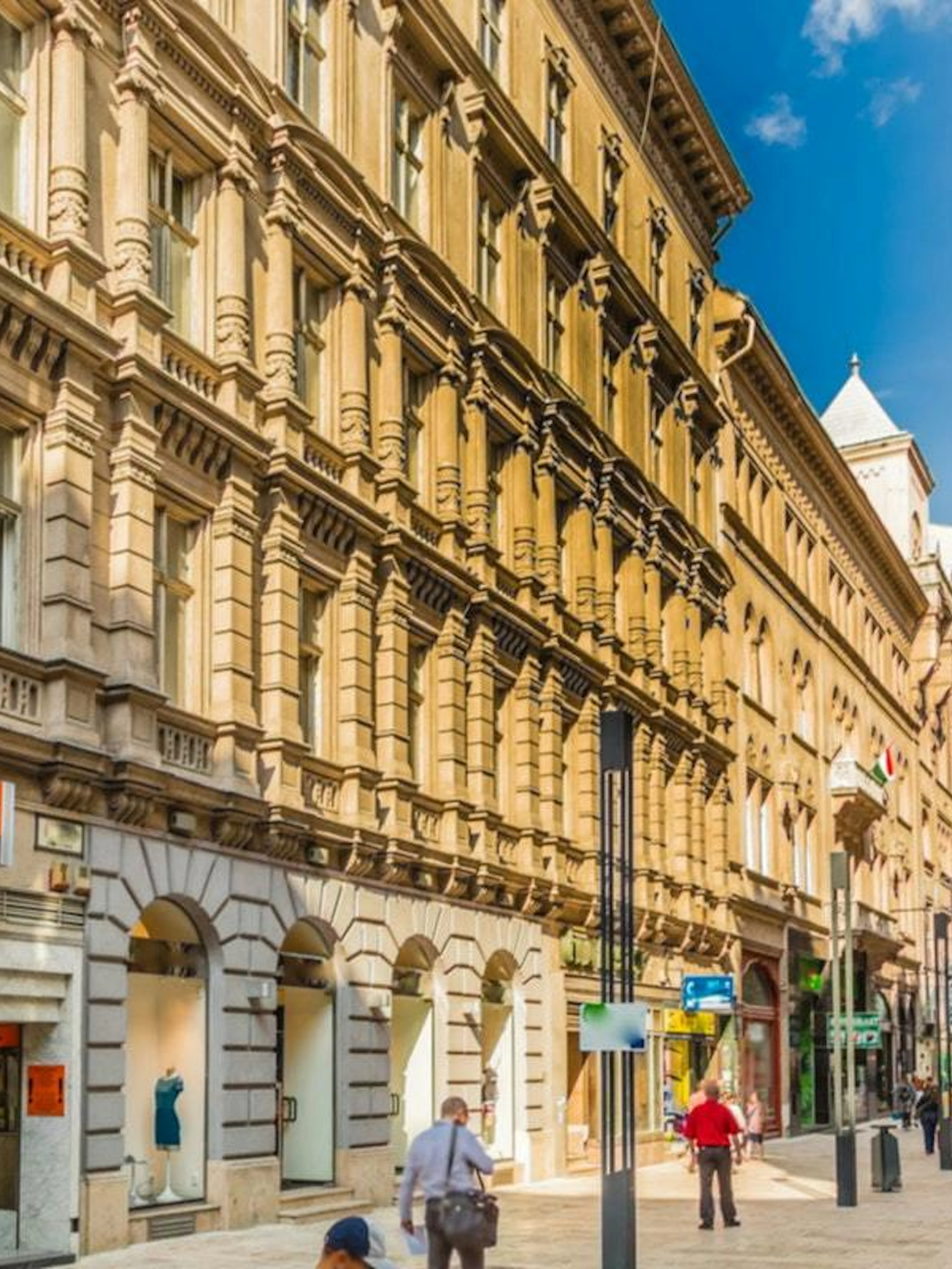 Pedestrians walking along a historic street in Budapest, part of the Supernatural Detective city exploration game.