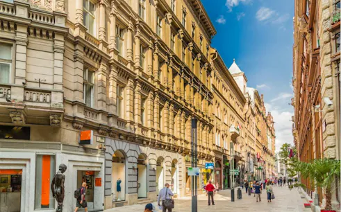 Pedestrians walking along a historic street in Budapest, part of the Supernatural Detective city exploration game.