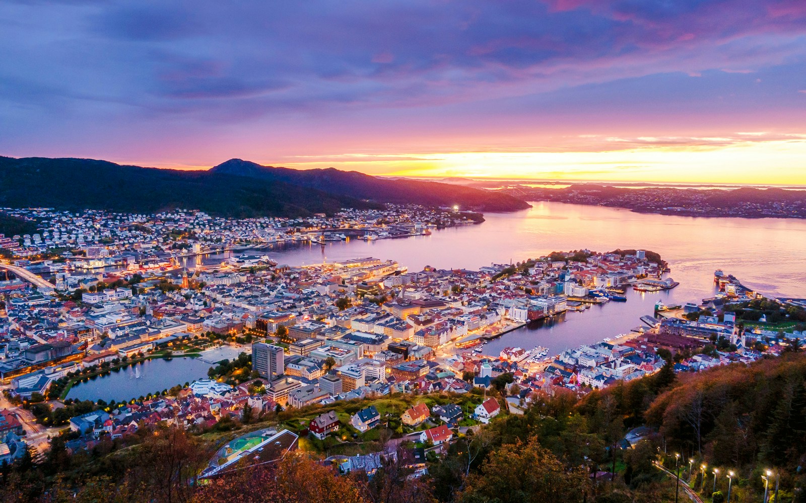 Aerial view of Bergen city at sunset with harbor and surrounding mountains.