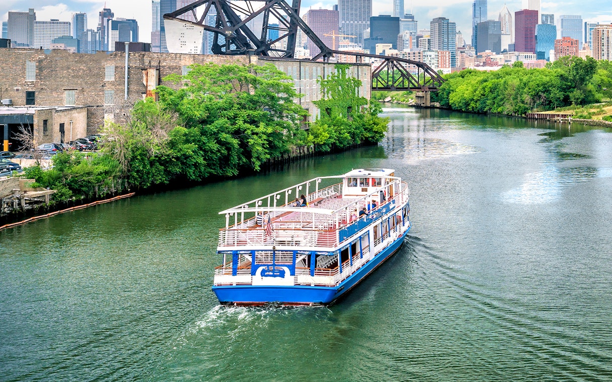 Tour boat cruising on the Chicago River with city skyline and bridge in the background.