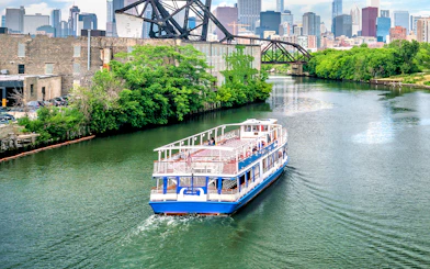 Tour boat cruising on the Chicago River with city skyline and bridge in the background.