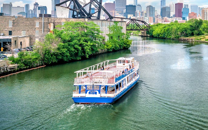 Tour boat cruising on the Chicago River with city skyline and bridge in the background.