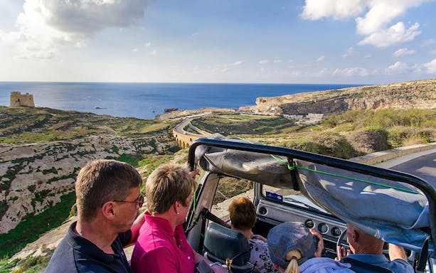 Tourists in a jeep exploring Gozo's coastal landscape with sea view.