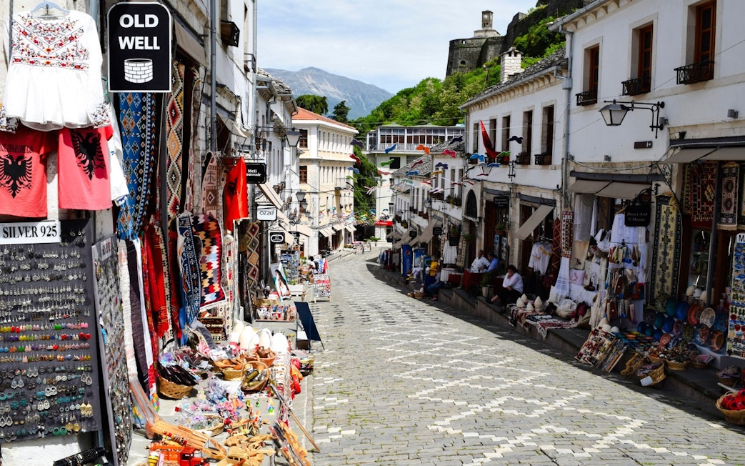 Gjirokaster Old Bazaar street with shops displaying traditional crafts and textiles.