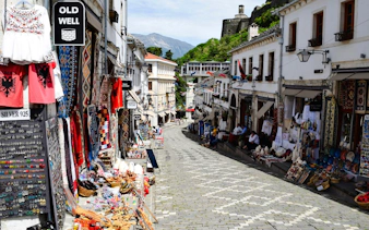 Gjirokaster Old Bazaar street with shops displaying traditional crafts and textiles.