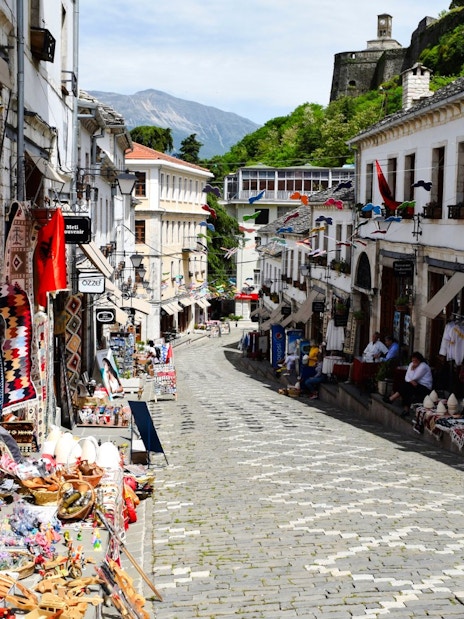 Gjirokaster Old Bazaar street with shops displaying traditional crafts and textiles.