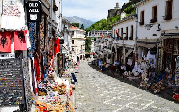 Gjirokaster Old Bazaar street with shops displaying traditional crafts and textiles.