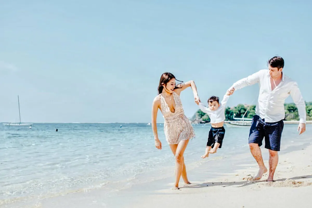 Family enjoying a beach photoshoot in Bali, with a child swinging between parents.