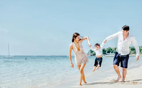 Family enjoying a beach photoshoot in Bali, with a child swinging between parents.