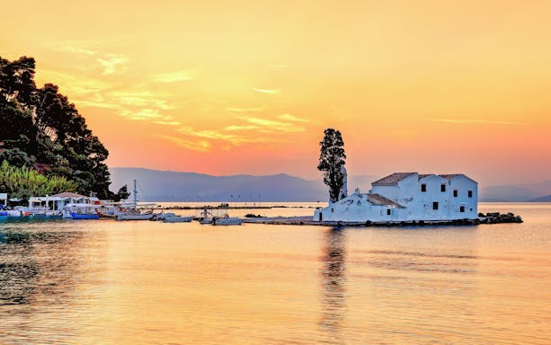 Sunset view of Panagia Vlacherna island with boats in Corfu, Greece.
