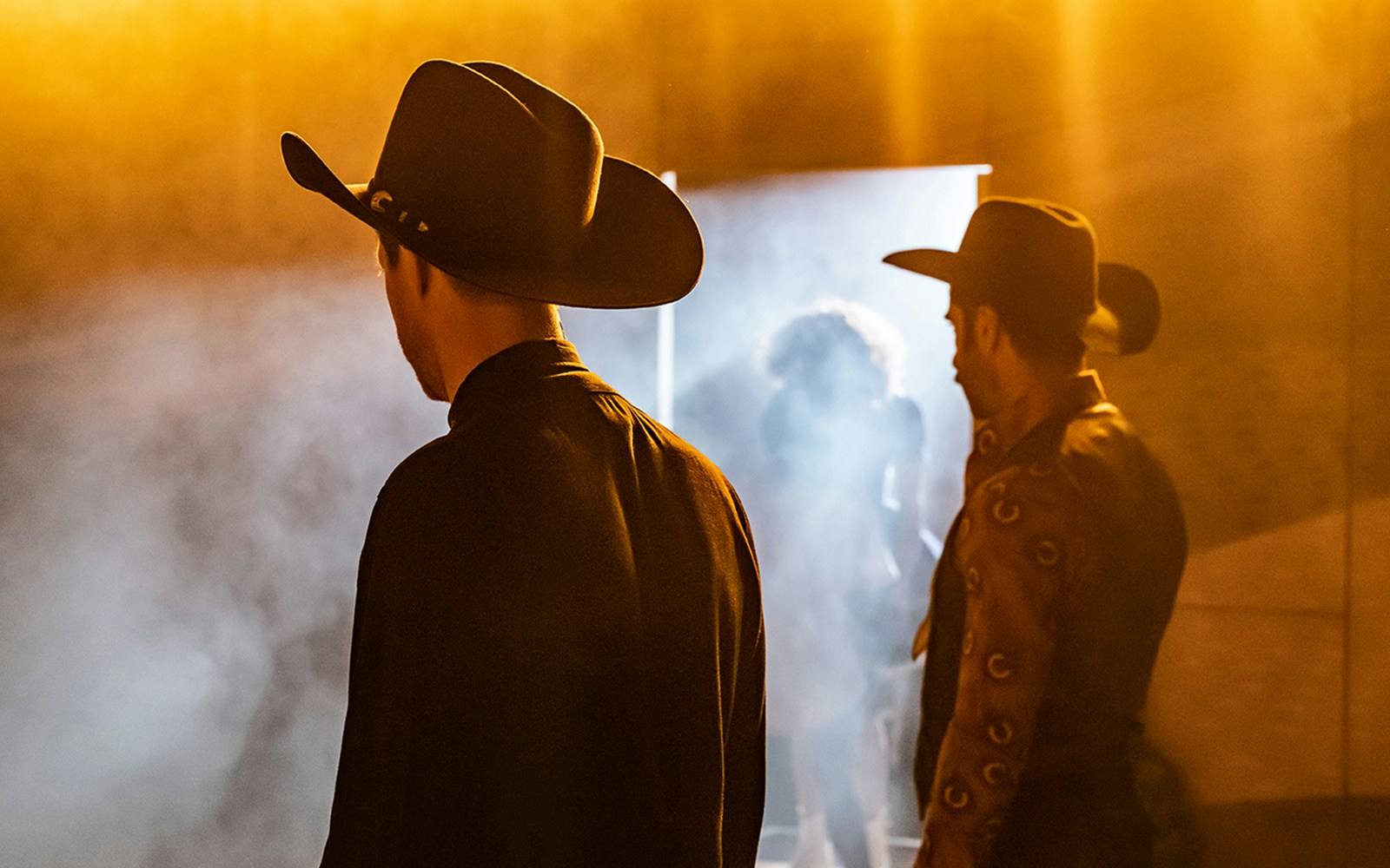 Cowboys in silhouette with stage lights and smoke, Oklahoma! performance.
