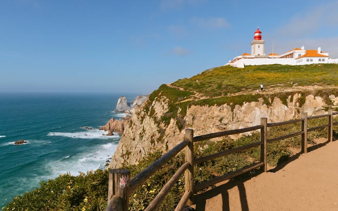 Cabo da Roca lighthouse on cliff overlooking the Atlantic Ocean during evening.