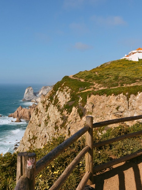 Cabo da Roca lighthouse on cliff overlooking the Atlantic Ocean during evening.