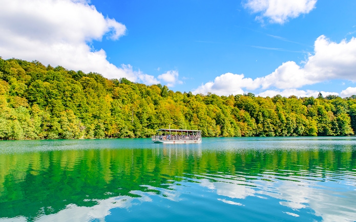 Boat on turquoise lake at Plitvice Lakes National Park with forest backdrop.