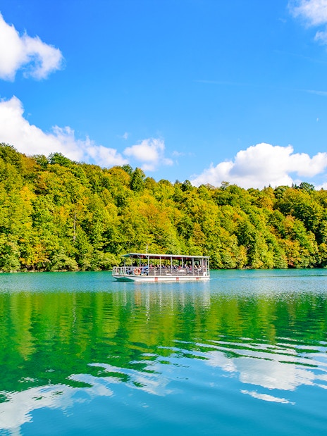 Boat on turquoise lake at Plitvice Lakes National Park with forest backdrop.