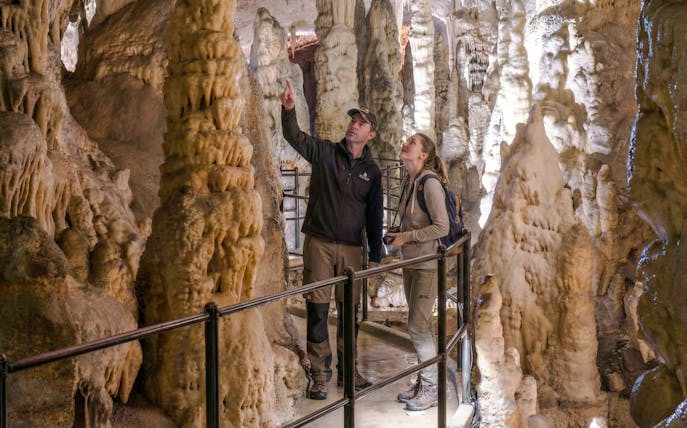 Tour guide explaining stalactites to visitor during Postojna Cave tour.