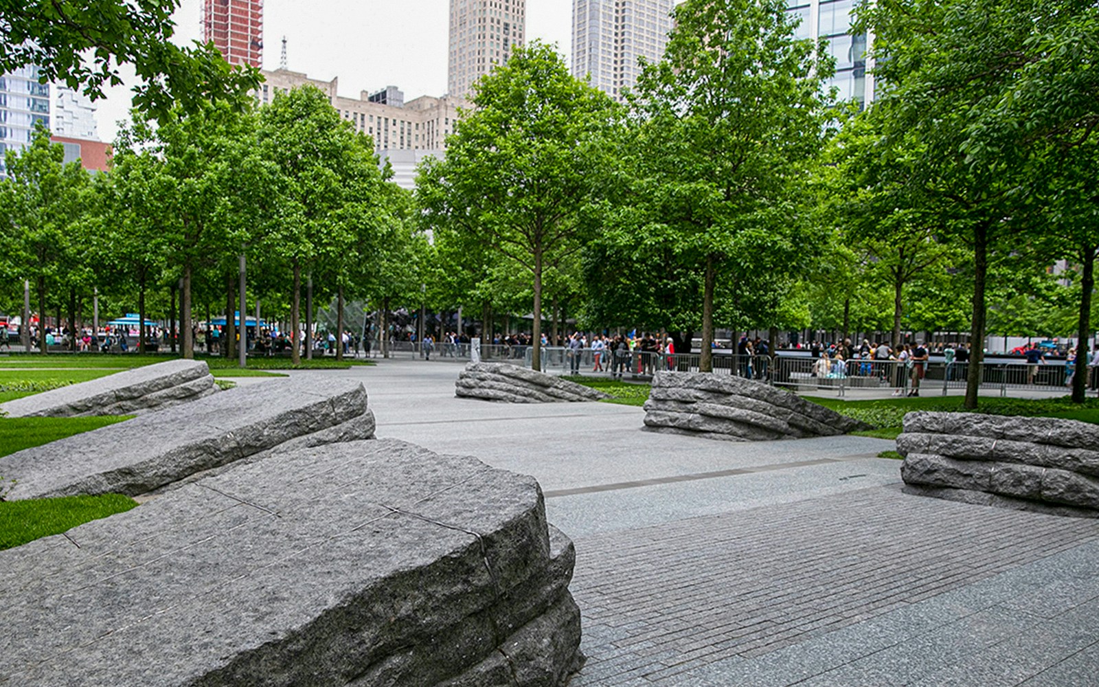 Visitors walking through the 9/11 Memorial Glade in New York City, surrounded by trees and stone monoliths.