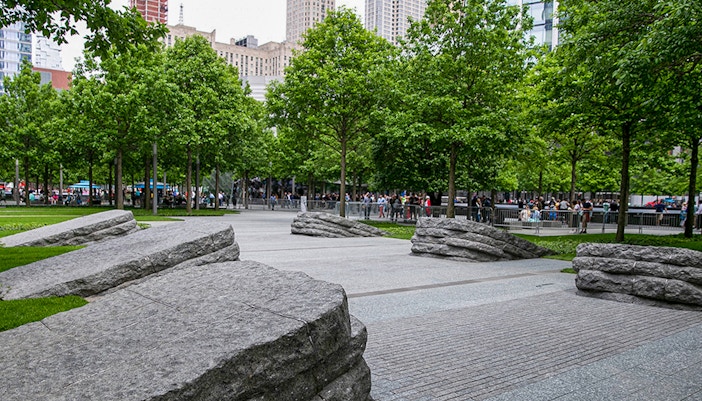 Visitors walking through the 9/11 Memorial Glade in New York City, surrounded by trees and stone monoliths.
