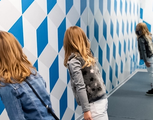 Visitors exploring a tilted room exhibit at the Museum of Illusions, Madrid.