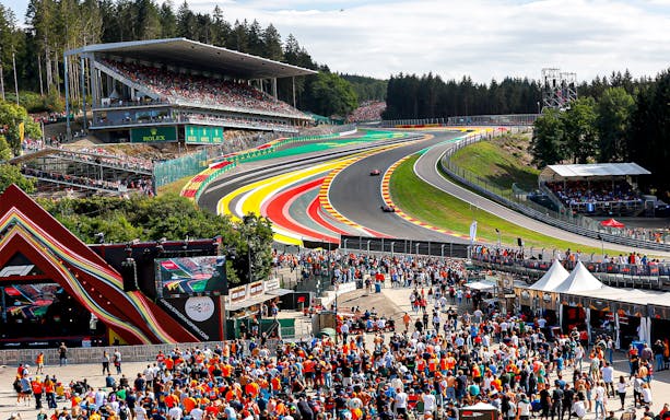 Crowd at Formula 1 Belgian Grand Prix, Spa-Francorchamps circuit, with cars on track.