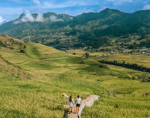 Couple walking through rice terraces in Sapa, Vietnam with mountains in the background.