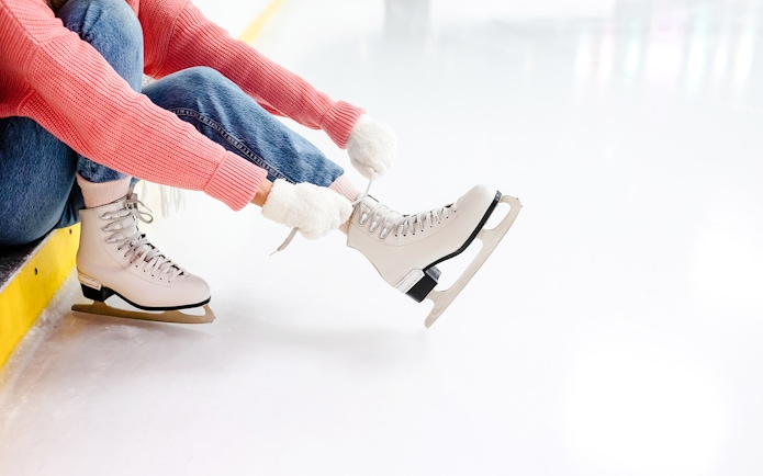 Young woman tying laces on ice skates at an ice rink.