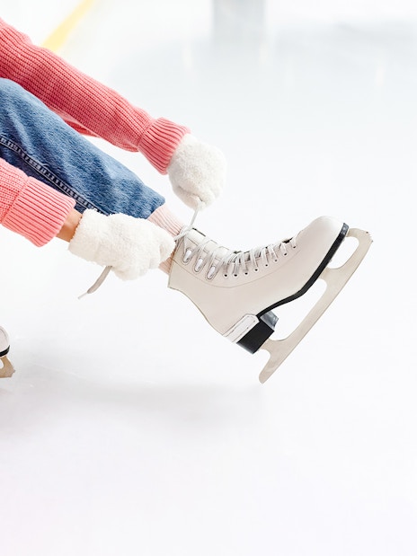 Young woman tying laces on ice skates at an ice rink.