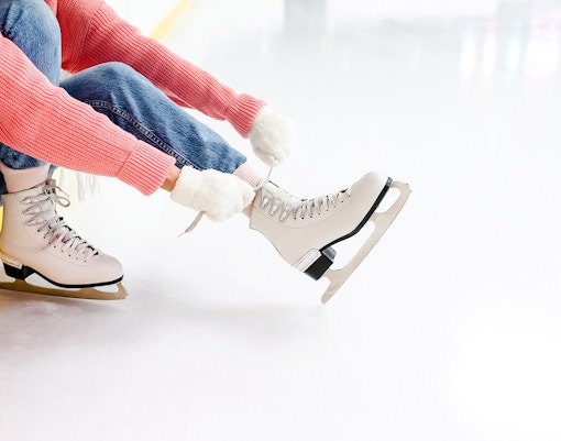 Young woman tying laces on ice skates at an ice rink.