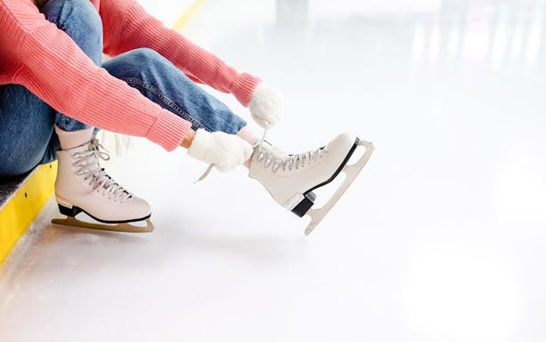 Young woman tying laces on ice skates at an ice rink.