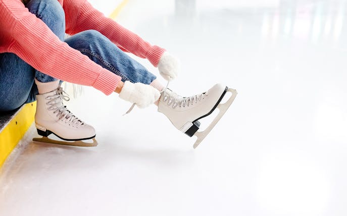 Young woman tying laces on ice skates at an ice rink.