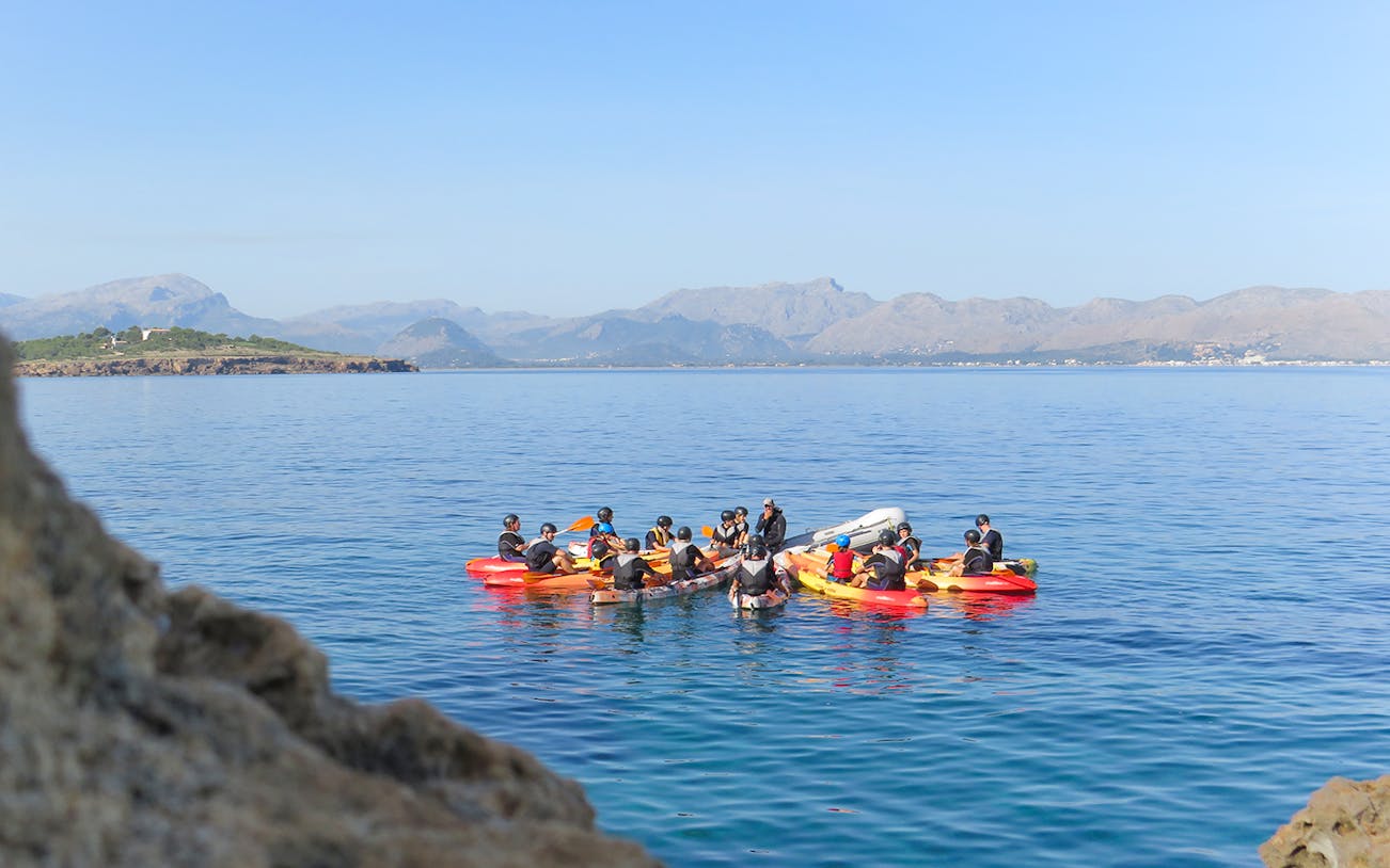 Group kayaking on clear waters with Mallorca mountains in the background.