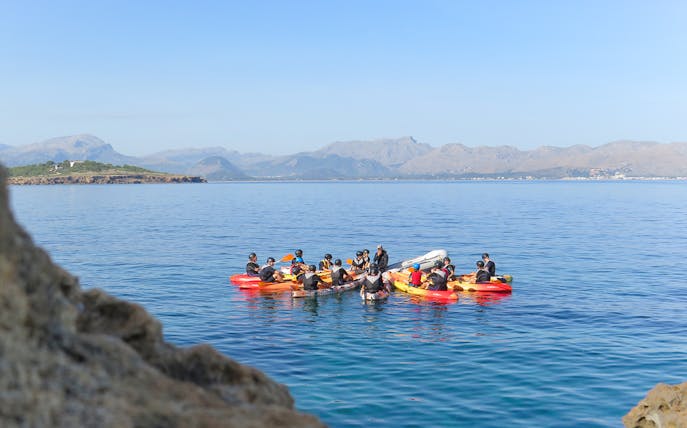 Group kayaking on clear waters with Mallorca mountains in the background.