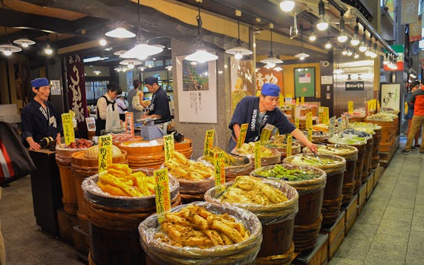 Vendors at Kyoto Nishiki Market arranging pickled vegetables in wooden barrels.