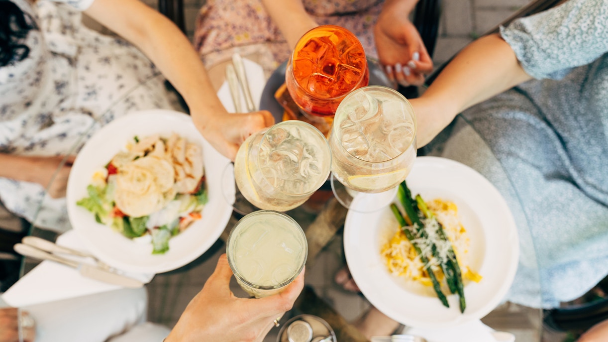 Tourists in Rome toasting with cocktails over plates of food.