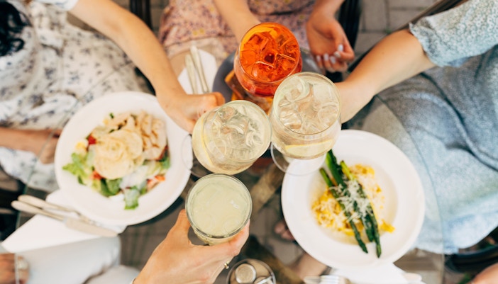 Tourists in Rome toasting with cocktails over plates of food.