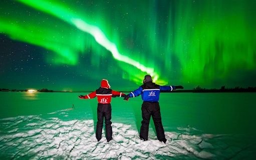 Two people in winter gear watching the Northern Lights in Rovaniemi.
