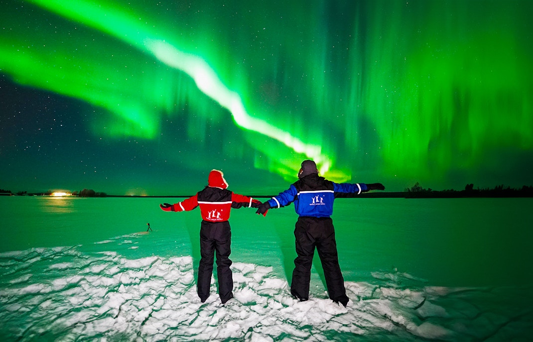 Two people in winter gear watching the Northern Lights in Rovaniemi.