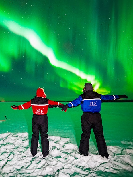 Two people in winter gear watching the Northern Lights in Rovaniemi.