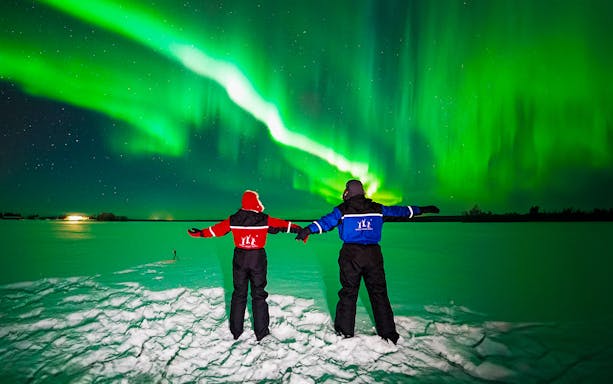 Two people in winter gear watching the Northern Lights in Rovaniemi.