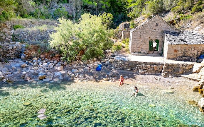 People enjoying the clear waters of Mala Stiniva bay near a rustic stone building.