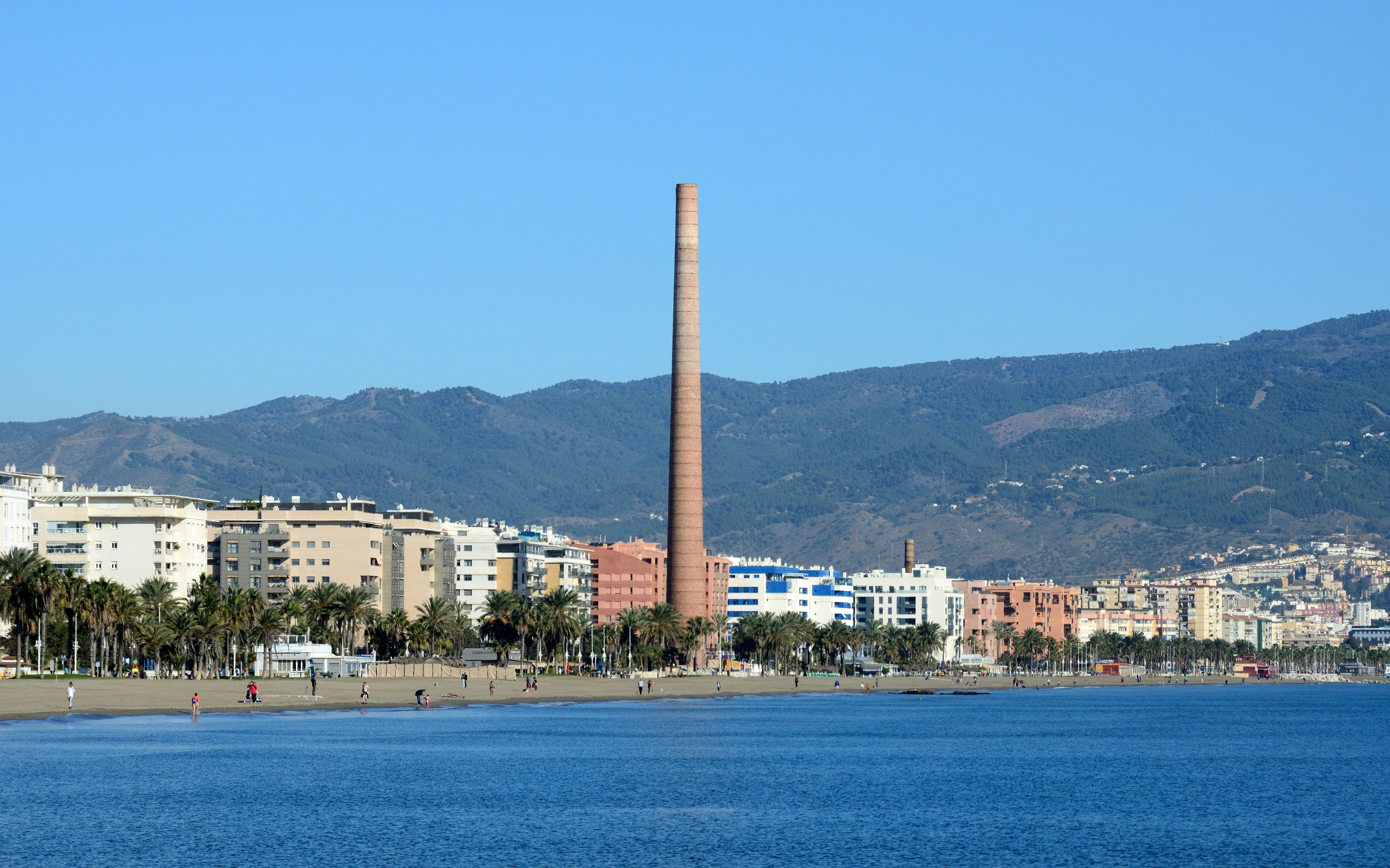 Misericordia Beach in Malaga with a tall chimney and cityscape in the background.