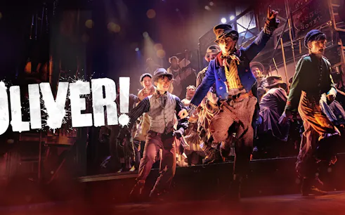 Performers dancing energetically on stage in the Oliver! show.