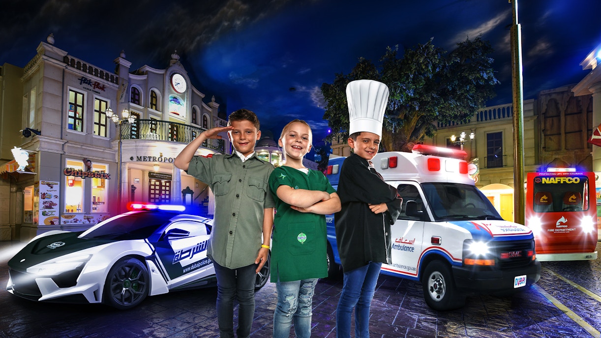 Children in uniforms at KidZania Dubai with police car and ambulance in background.