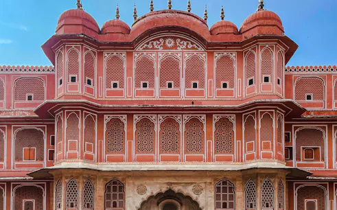 Facade of Jaipur's City Palace with intricate red and white latticework, part of Same Day Jaipur Tour from Delhi.