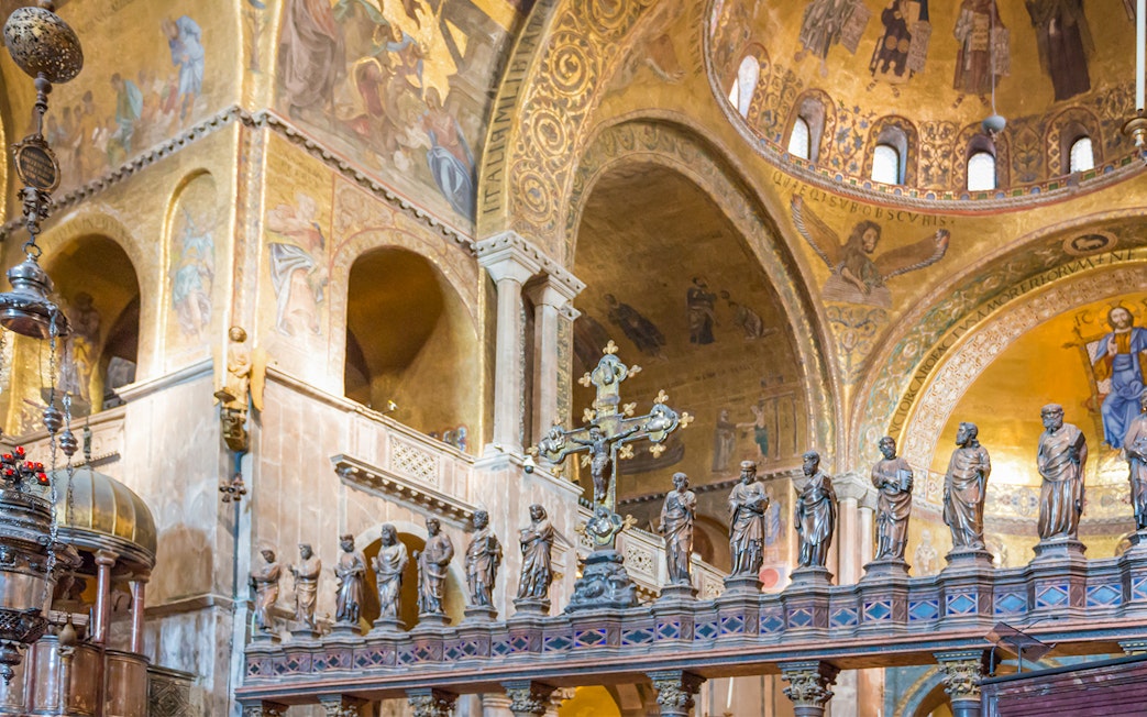 Interior of St. Mark's Basilica in Venice with ornate golden mosaics and statues.
