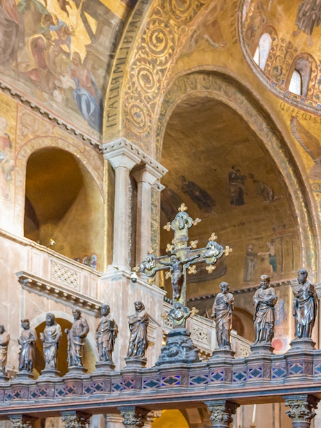Interior of St. Mark's Basilica in Venice with ornate golden mosaics and statues.